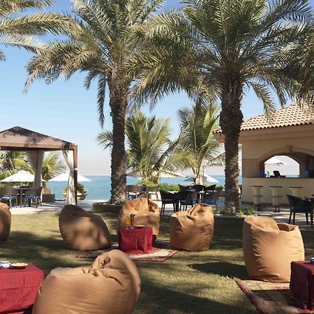 Al Raha Beach Resort & Spa Abu Dhabi Restoran foto The photo depicts a beautiful outdoor setting with several elements of relaxation and leisure. In the foreground, there are large, comfortable bean bag chairs arranged on a grassy area, accompanied by low tables. Surrounding this seating area are tal