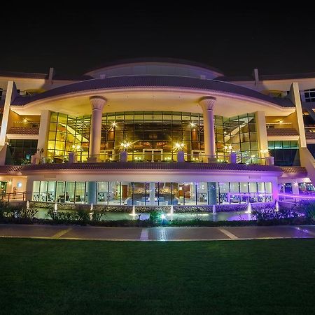 Al Raha Beach Resort & Spa Abu Dhabi Bagian luar foto The photo shows a modern architectural building illuminated at night. The structure has a large central entrance with multiple glass windows, flanked by symmetrical columns. The exterior features a combination of sleek lines and curves, with lighting