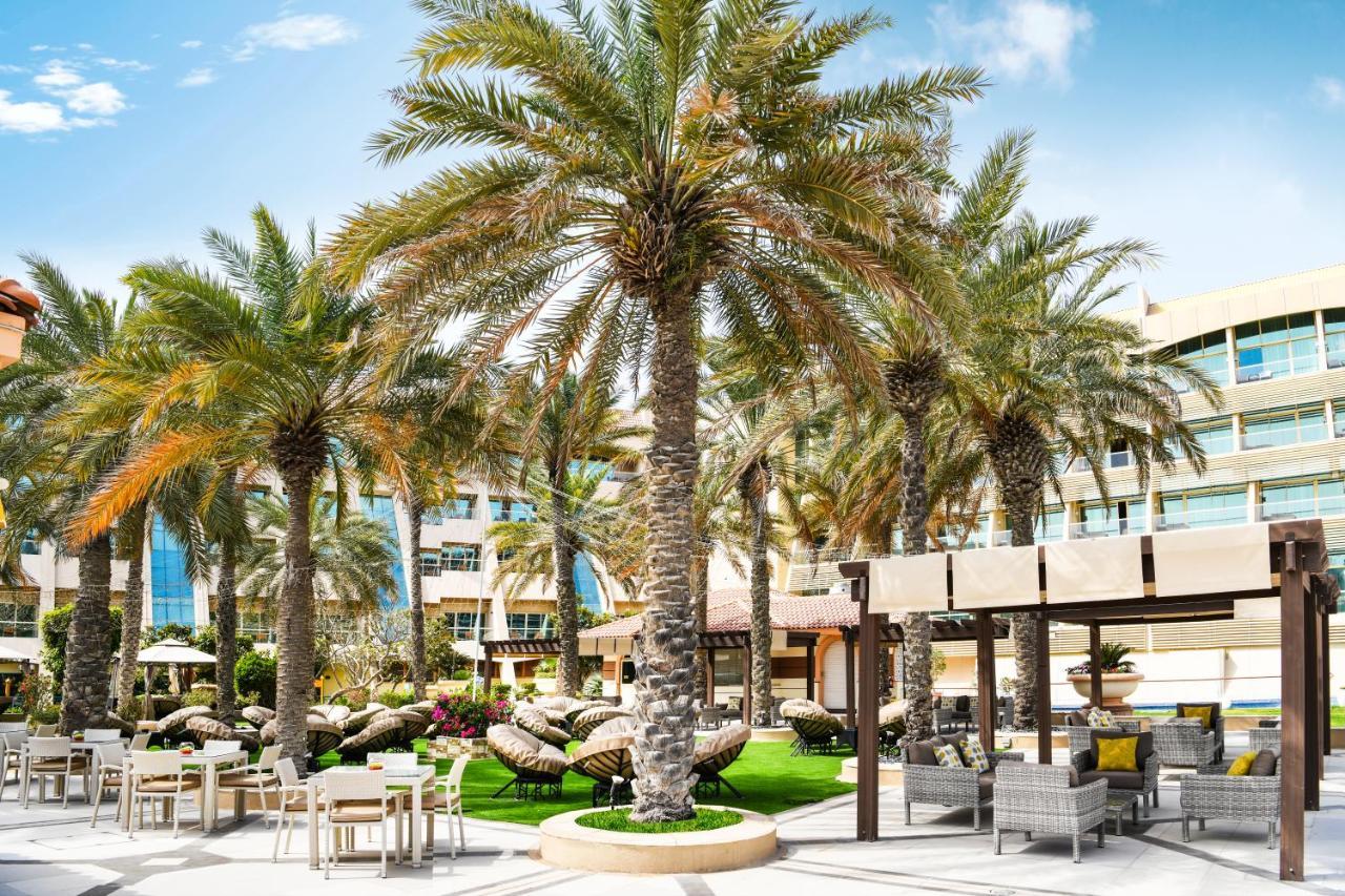 Al Raha Beach Resort & Spa Abu Dhabi Bagian luar foto The photo shows a picturesque outdoor area, likely at a resort or hotel. It features several tall palm trees that provide a tropical feel. In the foreground, there are several lounge chairs and seating arrangements, suggesting a relaxing environment.