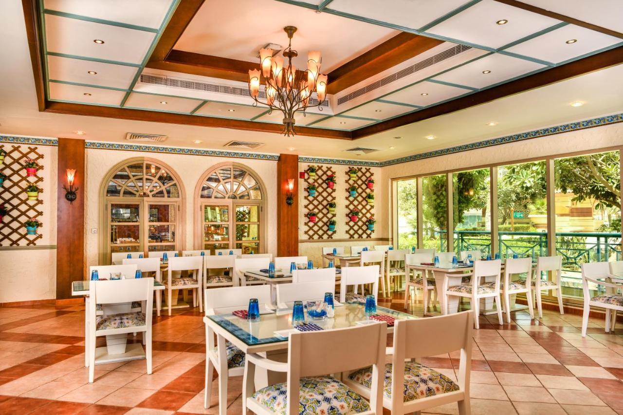 Al Raha Beach Resort & Spa Abu Dhabi Bagian luar foto The photo shows the interior of a restaurant or dining area. The space has a warm and inviting atmosphere, featuring a mix of decorative elements. 

- **Seating**: There are several white wooden tables and chairs arranged throughout the area, some wi