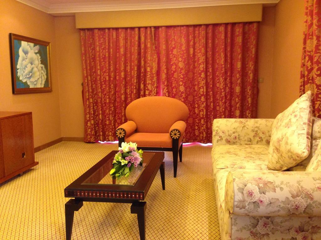 Al Raha Beach Resort & Spa Abu Dhabi Bagian luar foto The photo shows a cozy living room setting. There is an orange chair with decorative armrests situated near a floral-patterned sofa. A coffee table with a floral arrangement sits in front of the sofa. The room is adorned with warm colors, complementi