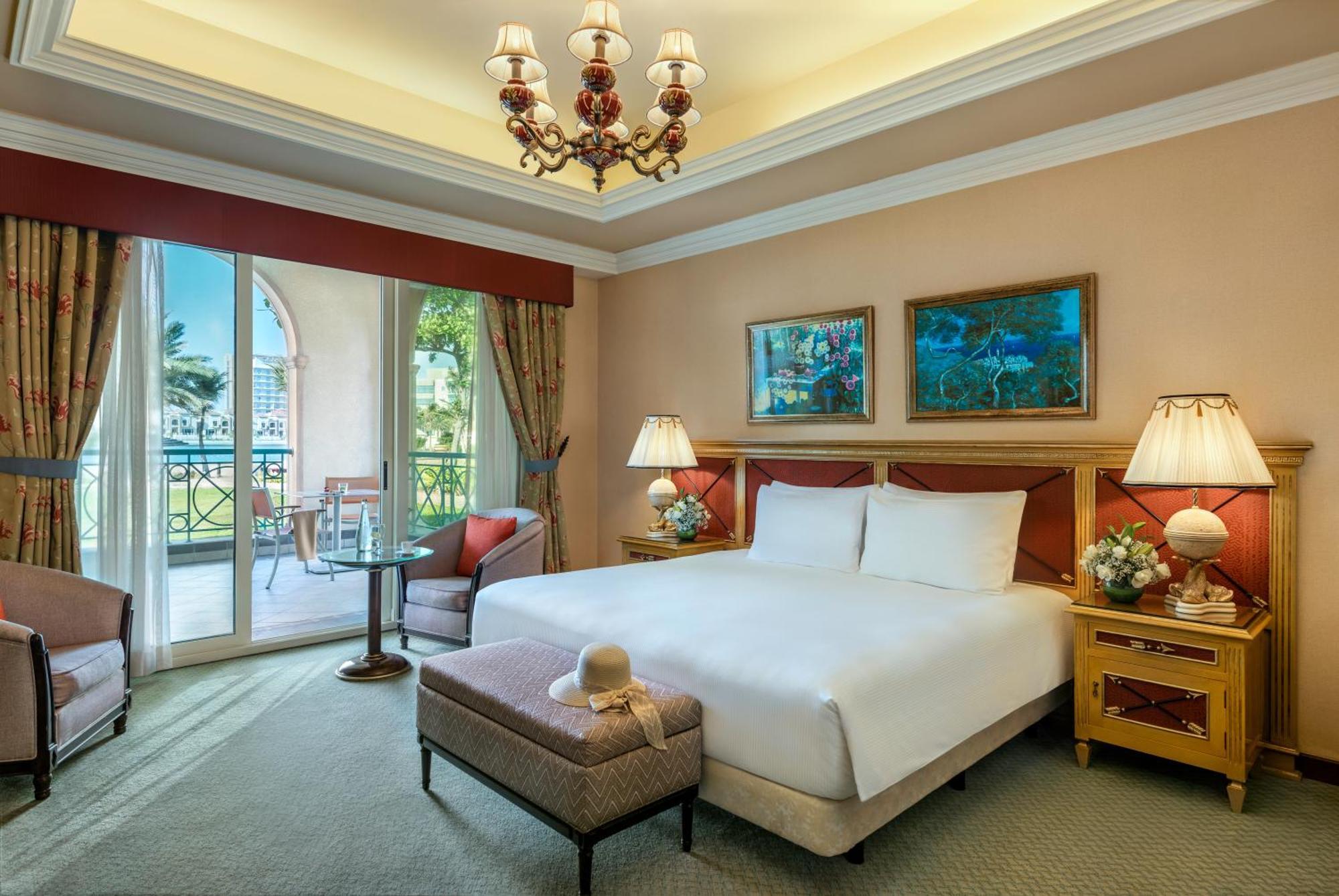 Al Raha Beach Resort & Spa Abu Dhabi Bagian luar foto The image depicts a well-furnished hotel room. It features a large bed with white linens, flanked by two bedside lamps. Above the bed, there are two pieces of artwork hanging on the walls. To the side, there is a comfortable armchair and a small tabl