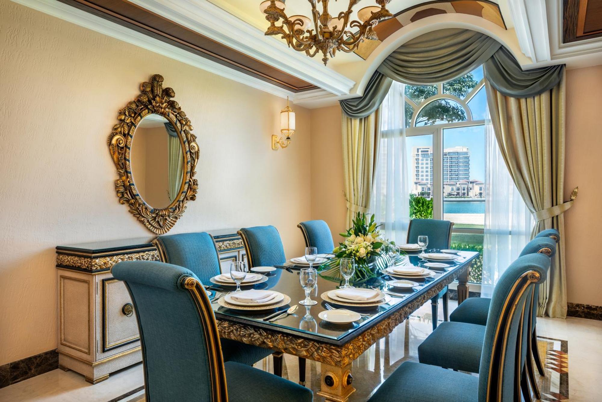Al Raha Beach Resort & Spa Abu Dhabi Bagian luar foto The photo features an elegantly decorated dining room. It includes a long, polished table set for a meal with plates, glasses, and decorative items, surrounded by plush blue chairs. The room is adorned with sophisticated details, such as an ornate mi