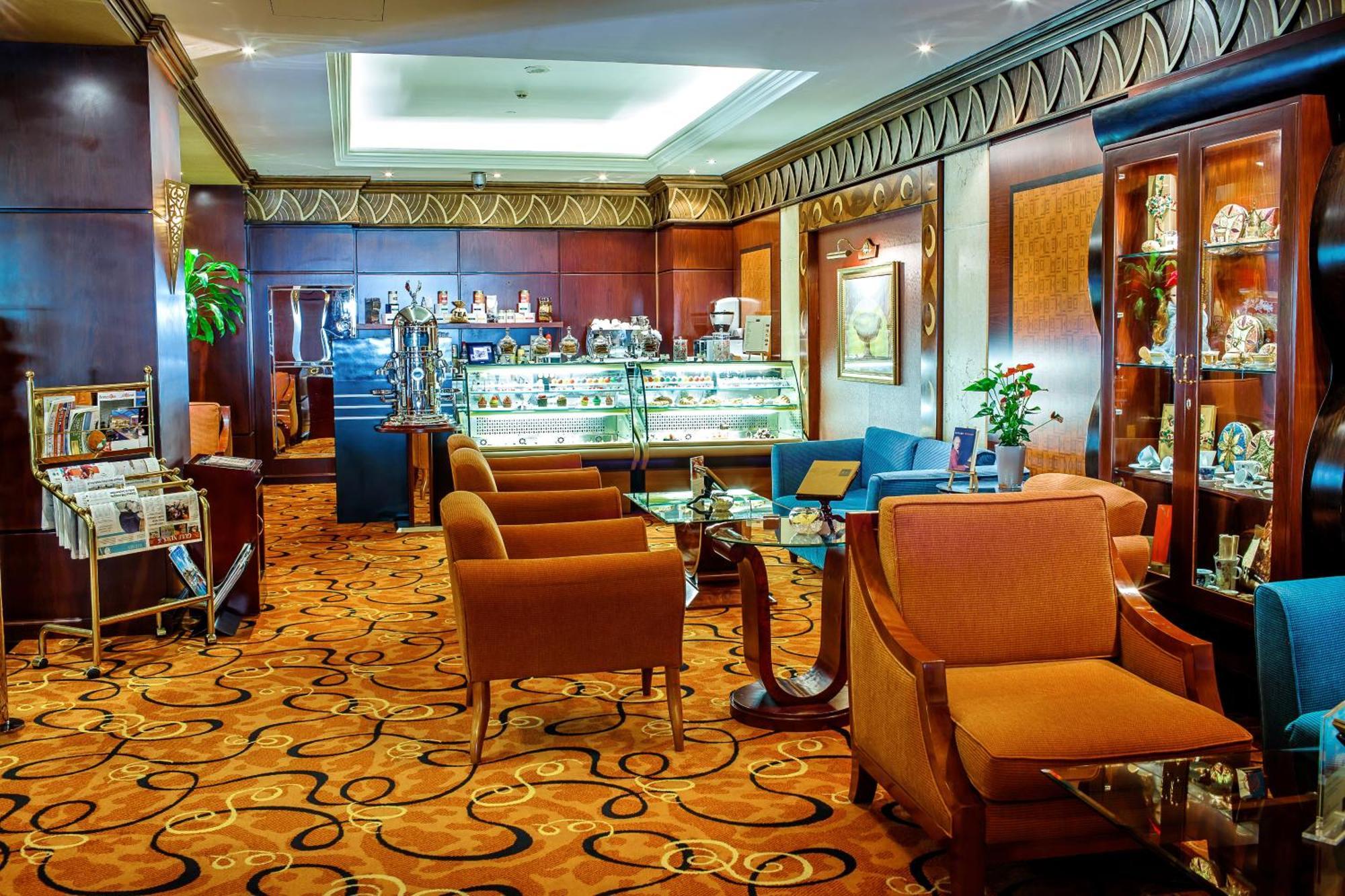 Al Raha Beach Resort & Spa Abu Dhabi Bagian luar foto The photo shows a cozy and elegantly designed lounge or café area. It features plush seating with brown armchairs and a blue couch. In the background, there is a display case filled with various items, likely including pastries or decorative goods. T