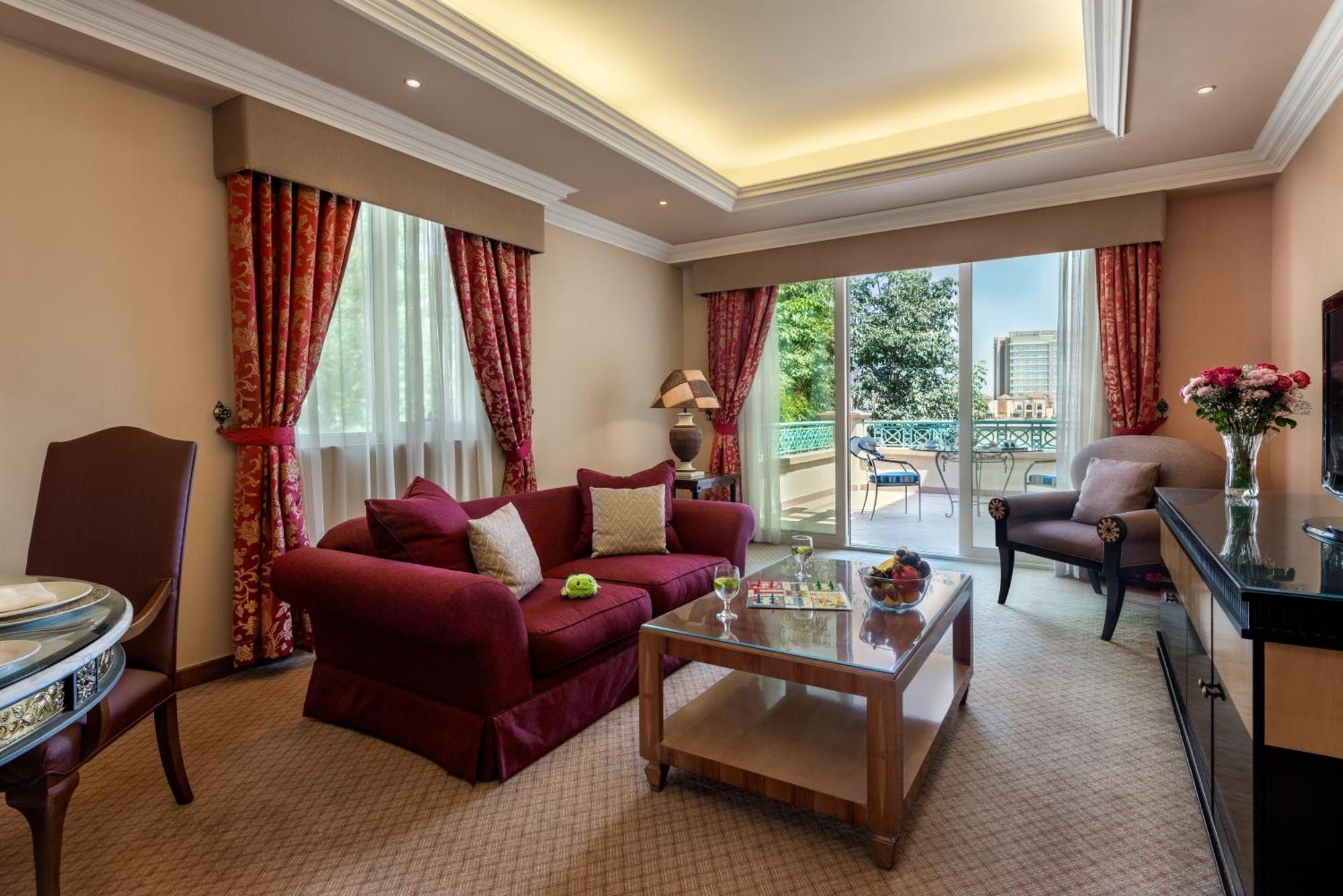 Al Raha Beach Resort & Spa Abu Dhabi Bagian luar foto The photo shows a well-decorated hotel room or living area. It features a cozy seating arrangement with a deep red couch adorned with cushions, paired with a single chair. There is a glass coffee table in front of the couch, which is set on a plush c