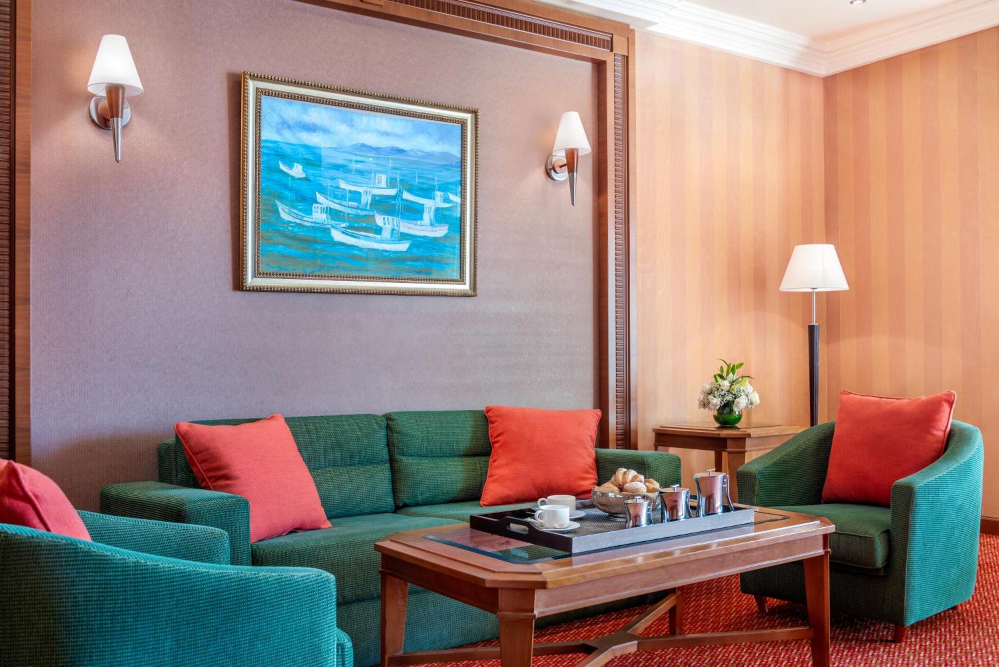 Al Raha Beach Resort & Spa Abu Dhabi Bagian luar foto The photo displays a cozy and elegantly furnished living area. It features a green sofa adorned with orange cushions and two matching green armchairs. A wooden coffee table sits in the center, which holds a tray with beverages and snacks. The walls a