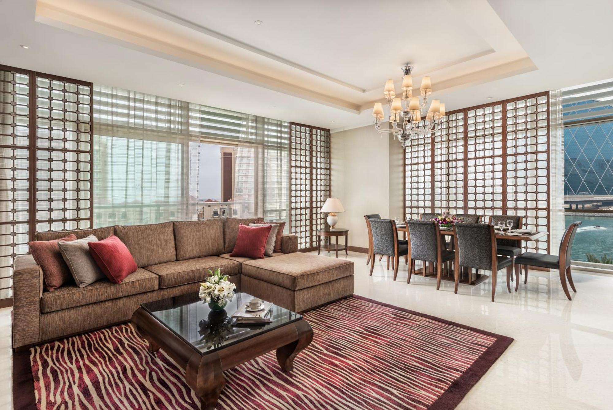 Al Raha Beach Resort & Spa Abu Dhabi Bagian luar foto The photo shows a stylish and modern living space. On one side, there is a comfortable sectional sofa in a brown upholstery, accented with red and gray cushions. In front of the sofa, there is a glossy black coffee table adorned with a small floral a
